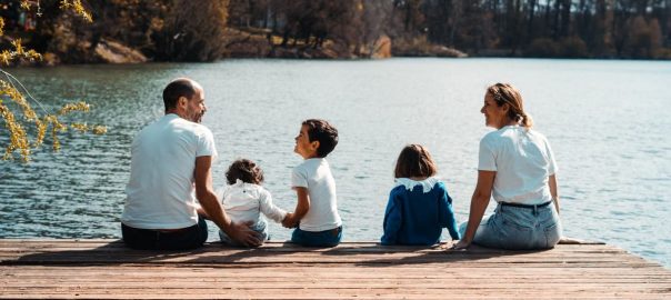 A family of five relaxing by a serene lake in Lyon, France on a sunny day.